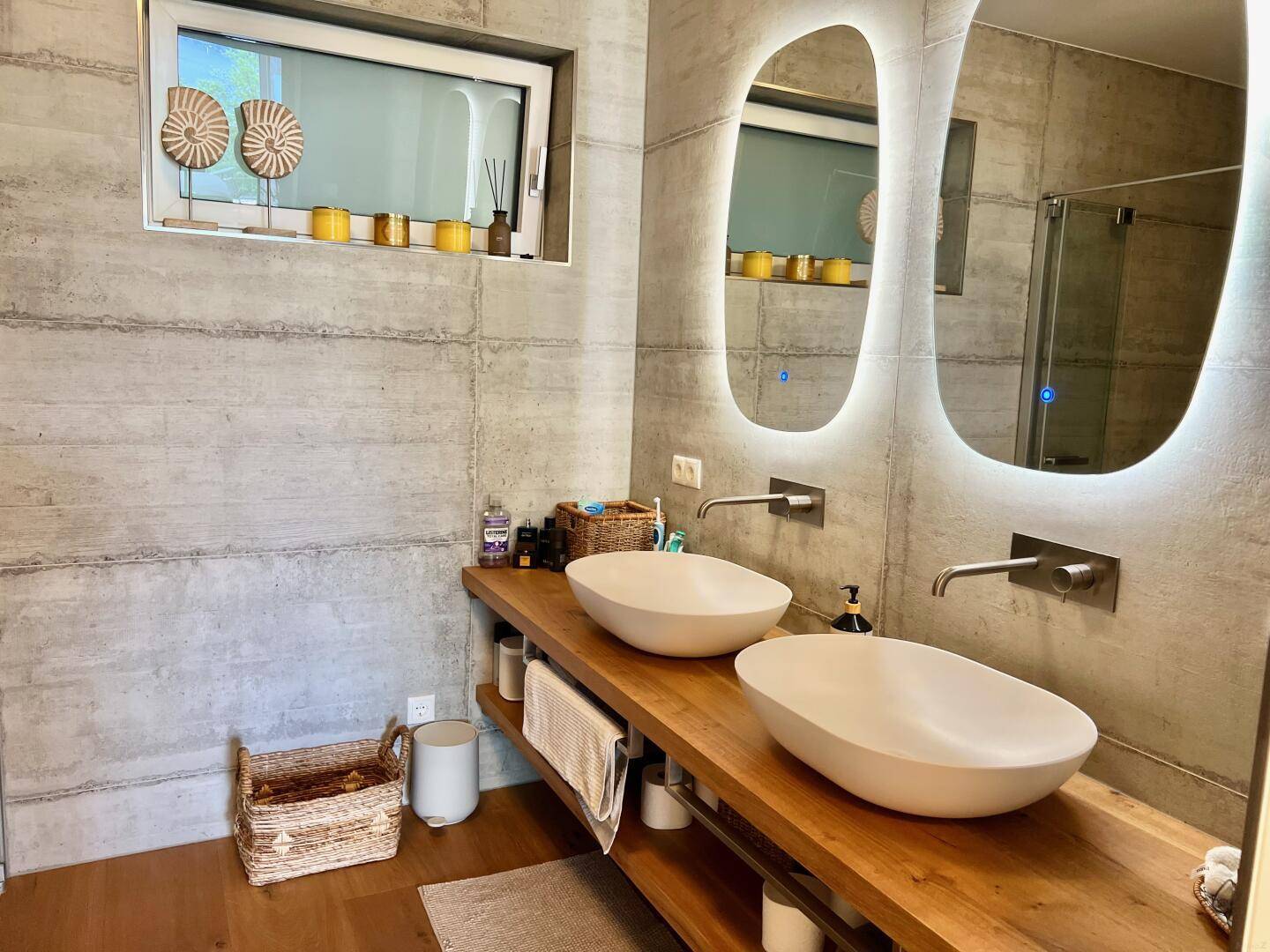 Modernes Badezimmer mit Doppelwaschbecken, beleuchteten Spiegeln und Fenster.
