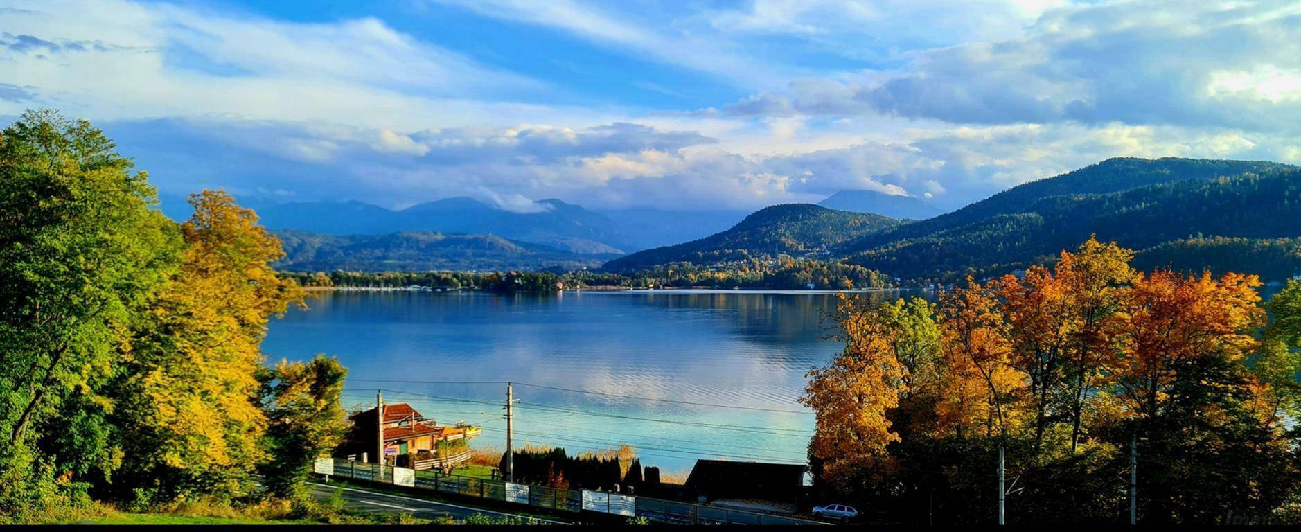 Malerischer Panoramablick auf einen See, umgeben von Bergen und herbstlichen Wäldern.