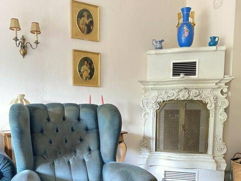 Gemütliches Wohnzimmer mit einem blauen Sessel und einem reich verzierten Kamin.