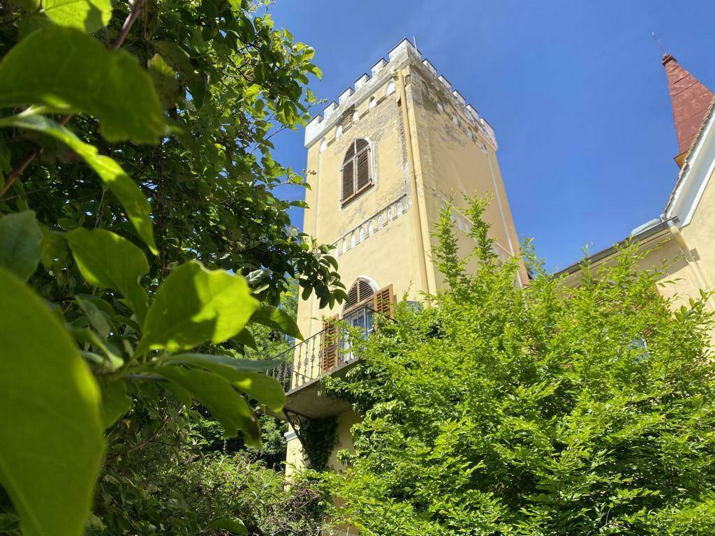 Historisches Gebäude mit einem markanten Turm und üppiger grüner Vegetation im Vordergrund.