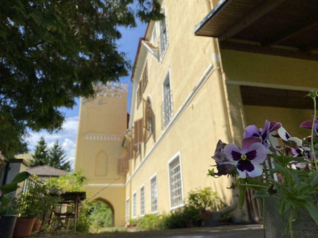 Gelbe Fassade eines historischen Gebäudes mit vielen Fenstern und blühenden Blumen im Vordergrund.