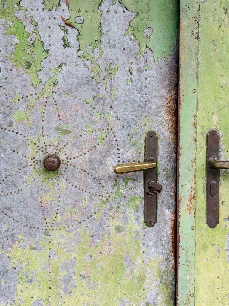 Alte, verwitterte Metalltür mit Patina und traditionellen Türgriffen in Grün- und Grautönen.