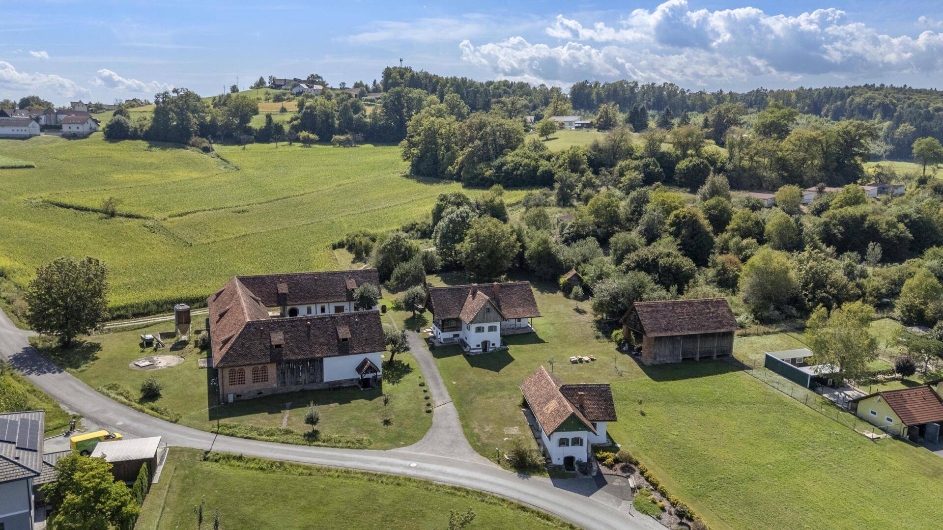 Weitläufiges ländliches Anwesen mit mehreren Gebäuden, umgeben von grünen Feldern und Bäumen.