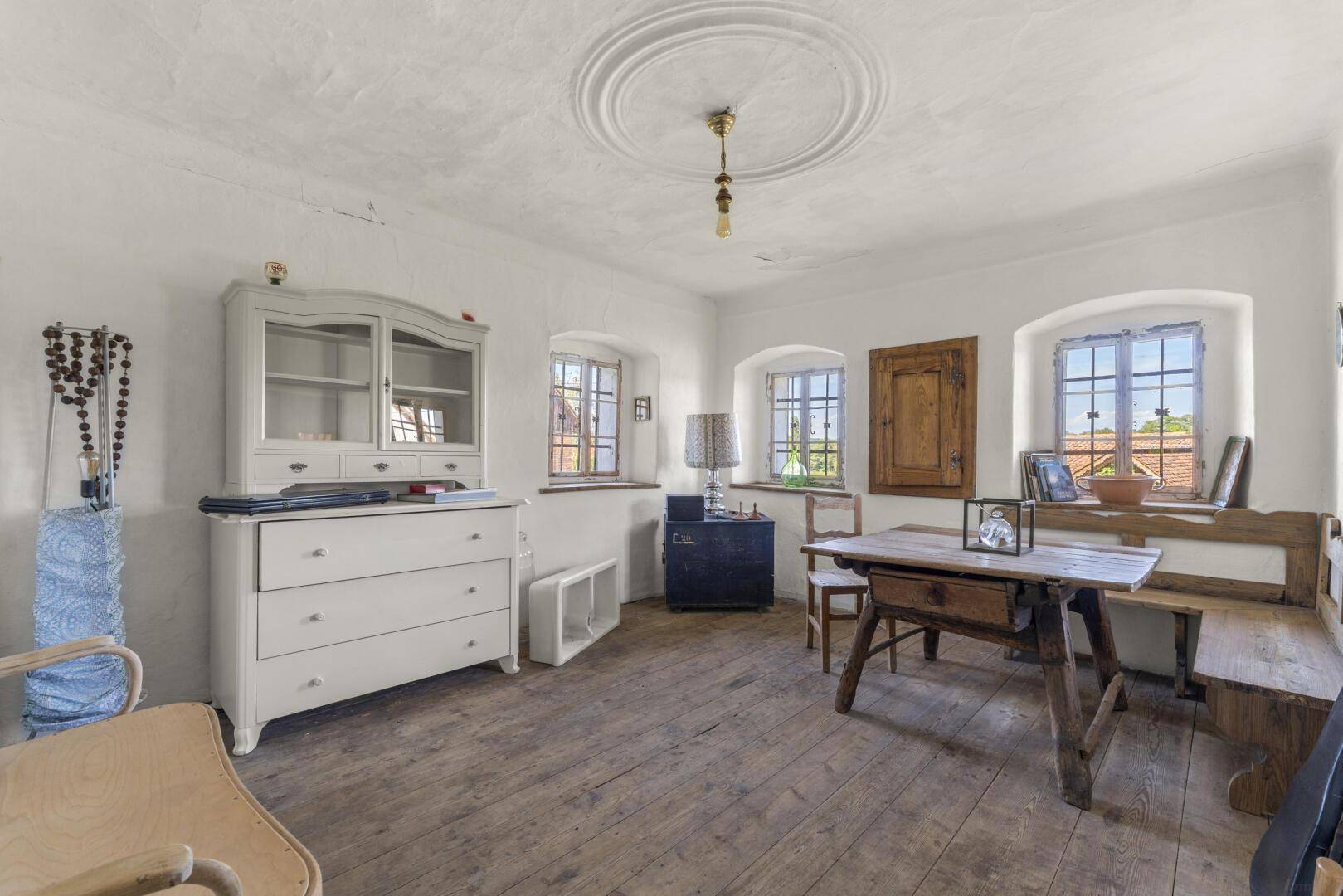 Heller Raum mit Holzdielenboden, traditionellen Möbeln und einem Stuckmedaillon an der Decke.