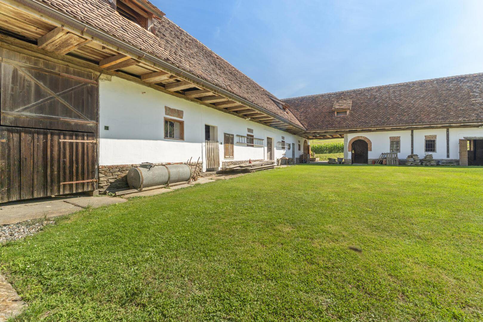 Innenhof eines historischen Anwesens mit gepflegtem Rasen und traditionellen Scheunentoren.