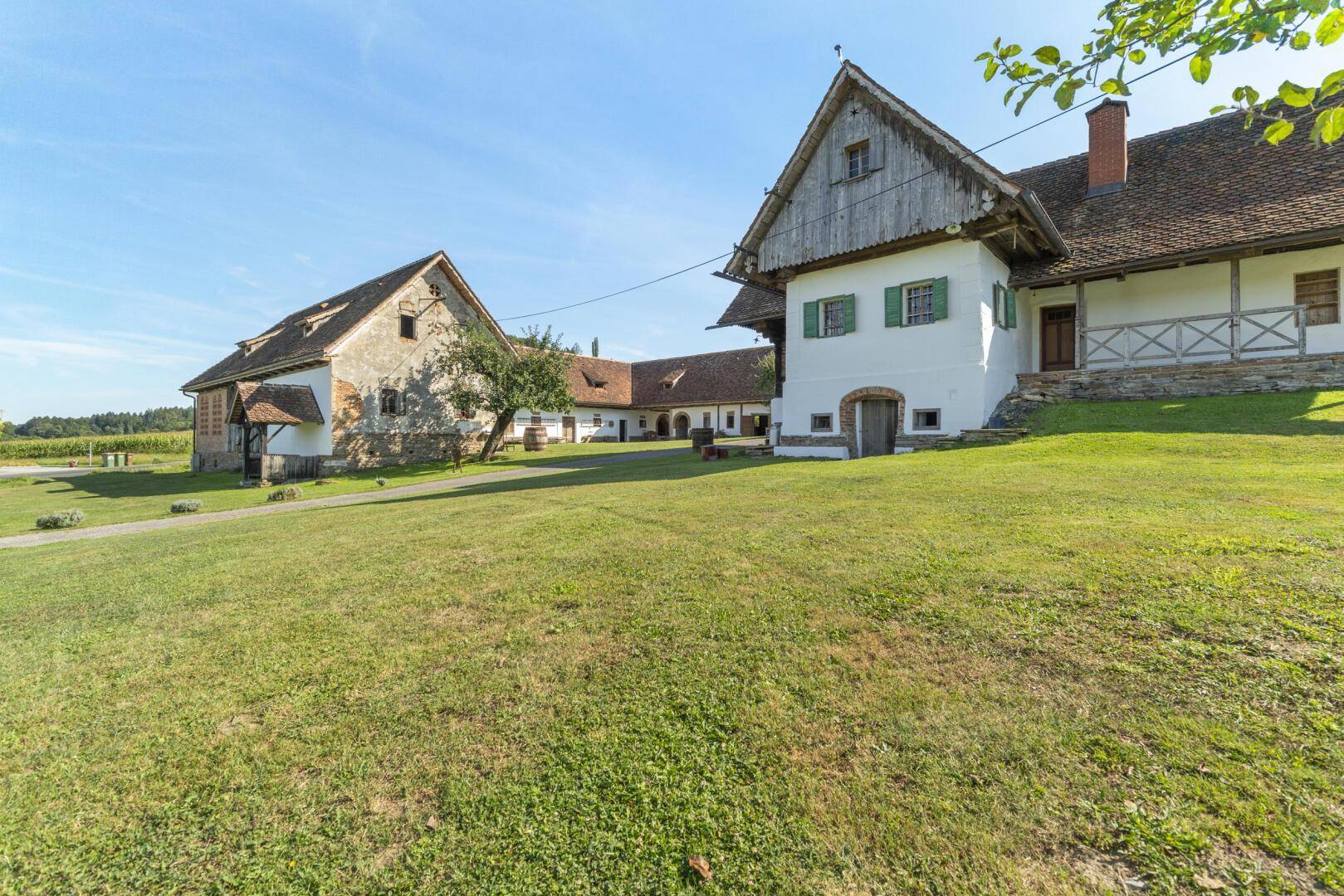 Traditionelle Bauernhäuser mit weiß getünchten Wänden und grünen Fensterläden, umgeben von einer weitläufigen Rasenfläche.