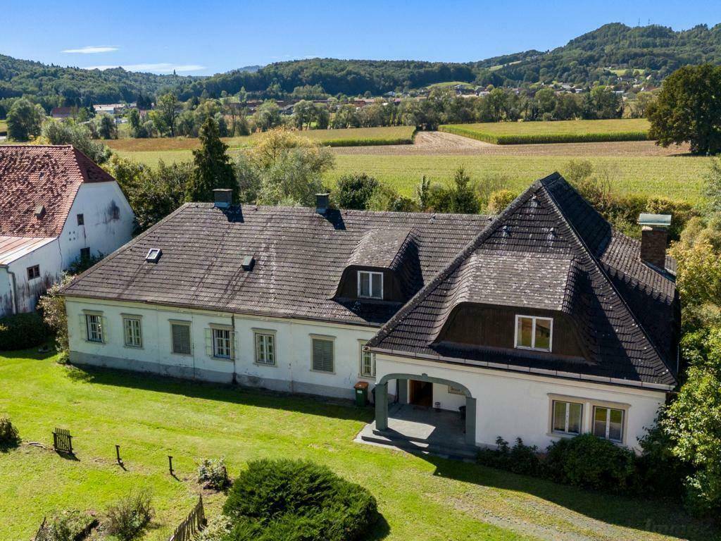 Großes Landhaus mit Mansarddach und gepflegtem Rasen, umgeben von grüner Landschaft.