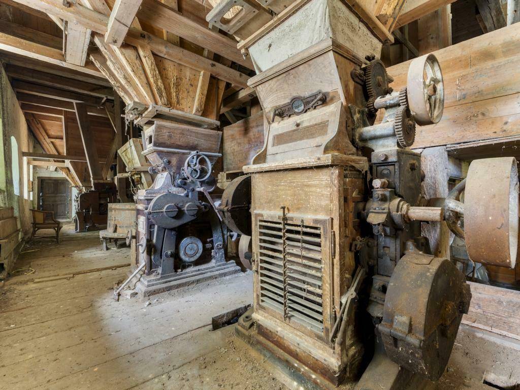 Detailansicht historischer Mühlenmaschinen aus Holz und rostigem Metall in einem alten Gebäude.