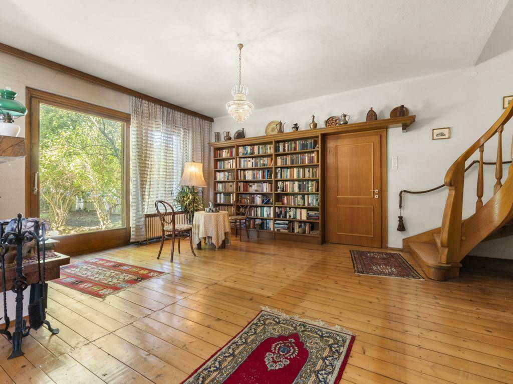 Heller Wohnbereich mit Holzdielenboden, Bücherregal und Treppe, die in eine obere Etage führt.