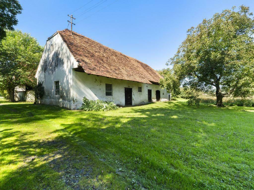 Altes Bauernhaus mit Ziegeldach und weiß getünchten Wänden, umgeben von Bäumen und Wiese.