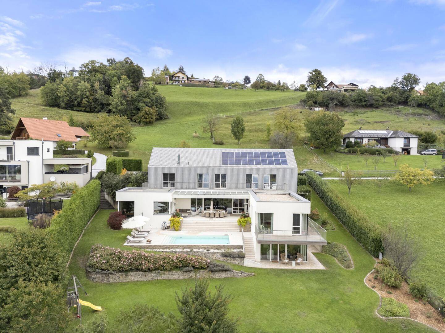 Moderne Villa mit Pool, weitläufigem Garten und grüner Hügellandschaft im Tageslicht.