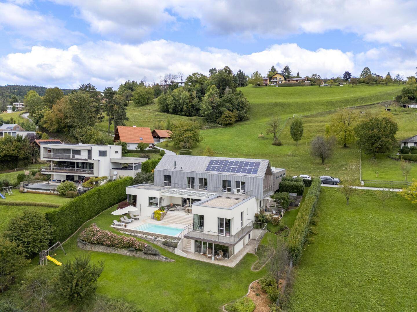 Weitläufige Ansicht der modernen Villa mit Pool und Garten in einer grünen Hügellandschaft.