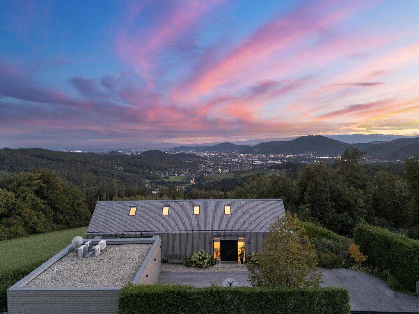 Panoramablick auf die moderne Villa mit Stadtblick und malerischem Sonnenuntergangshimmel.