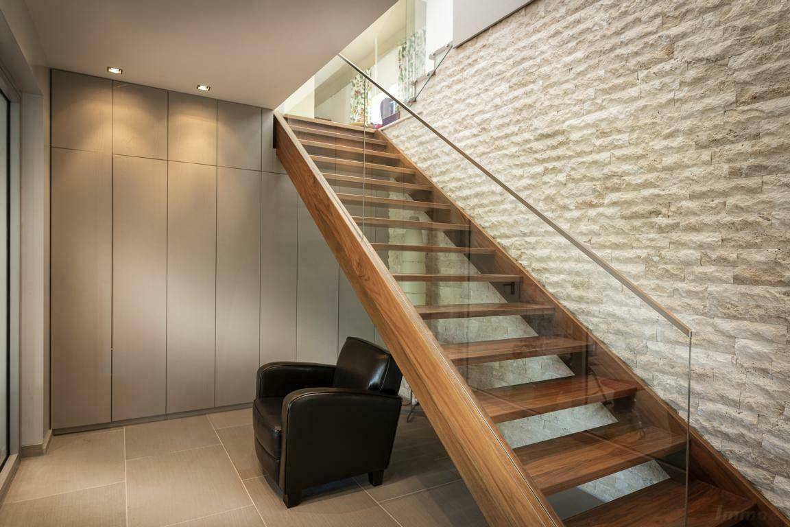 Moderner Eingangsbereich mit Holztreppe, Glasgeländer und einer Wandverkleidung aus Naturstein.