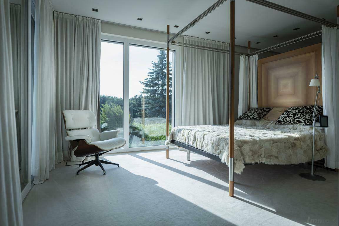 Geräumiges Schlafzimmer mit Himmelbett, hellem Teppichboden und großen Fenstern mit Blick ins Grüne.