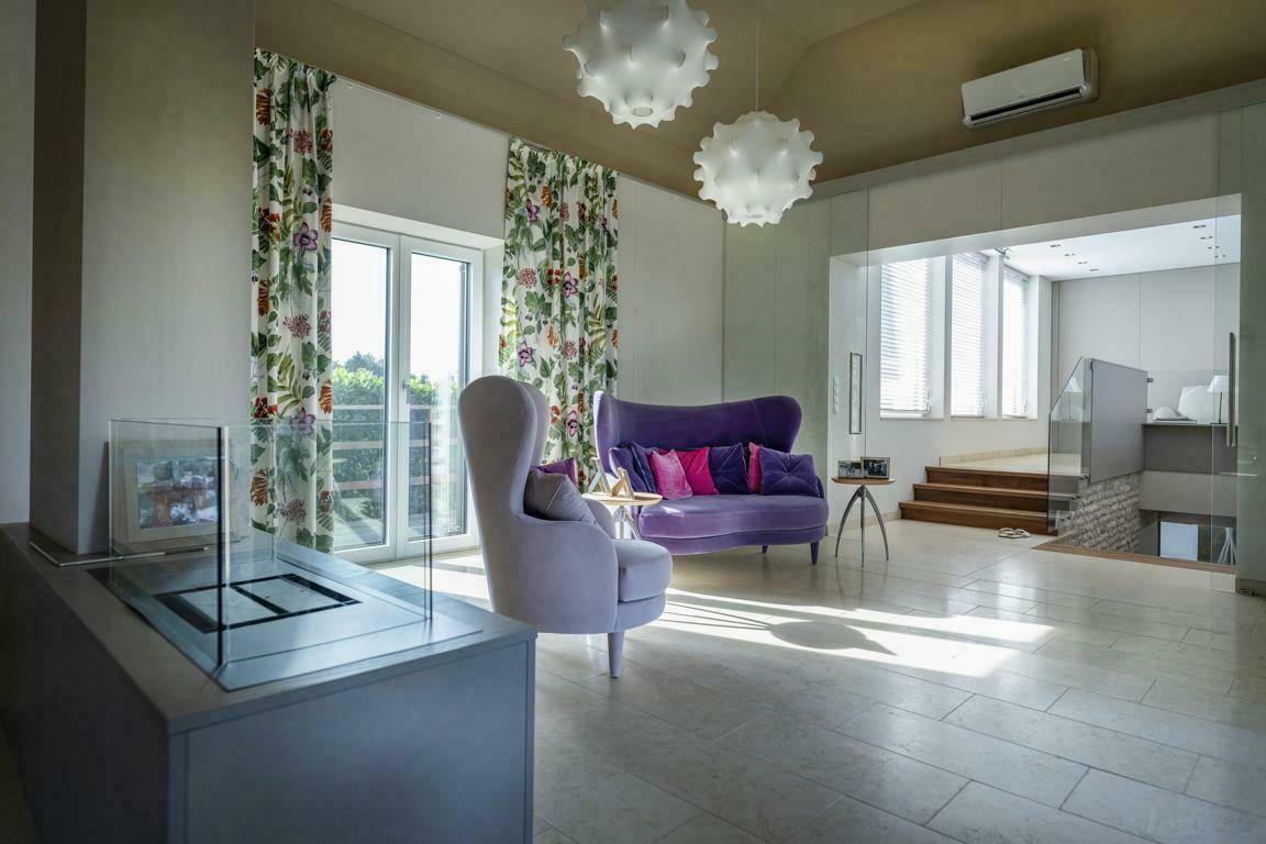 Helles Wohnzimmer mit farbenfrohen Möbeln, großen Fenstern und Zugang zu einem weiteren Bereich.