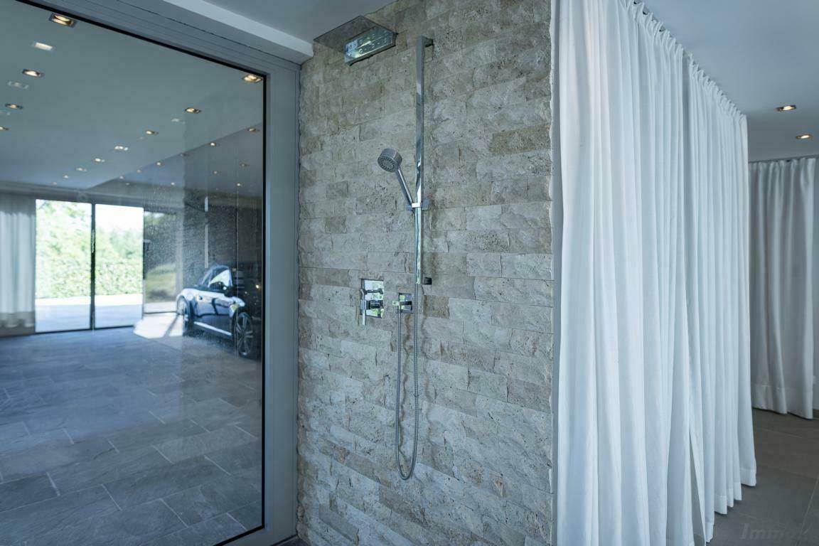 Moderne Dusche mit Natursteinwand und Glasabtrennung, angrenzend an einen offenen Bereich.