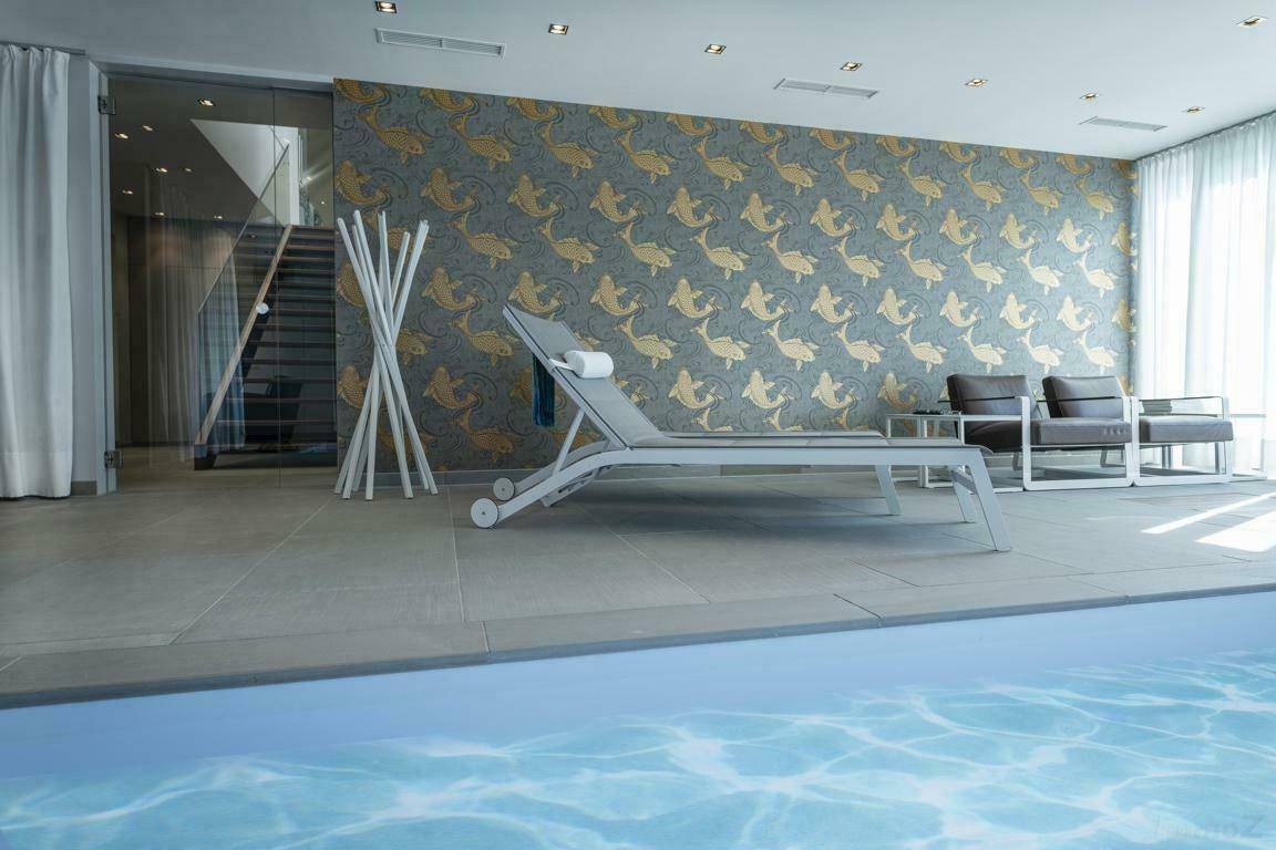 Innenpoolbereich mit Liegestühlen, dekorativer Wandgestaltung und Blick auf eine Treppe.