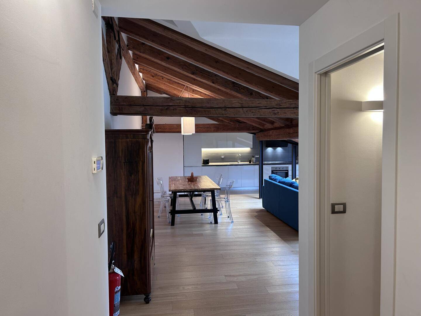Blick vom Flur in den offenen Wohnbereich mit Küche und Esszimmer unter rustikalen Holzbalken.