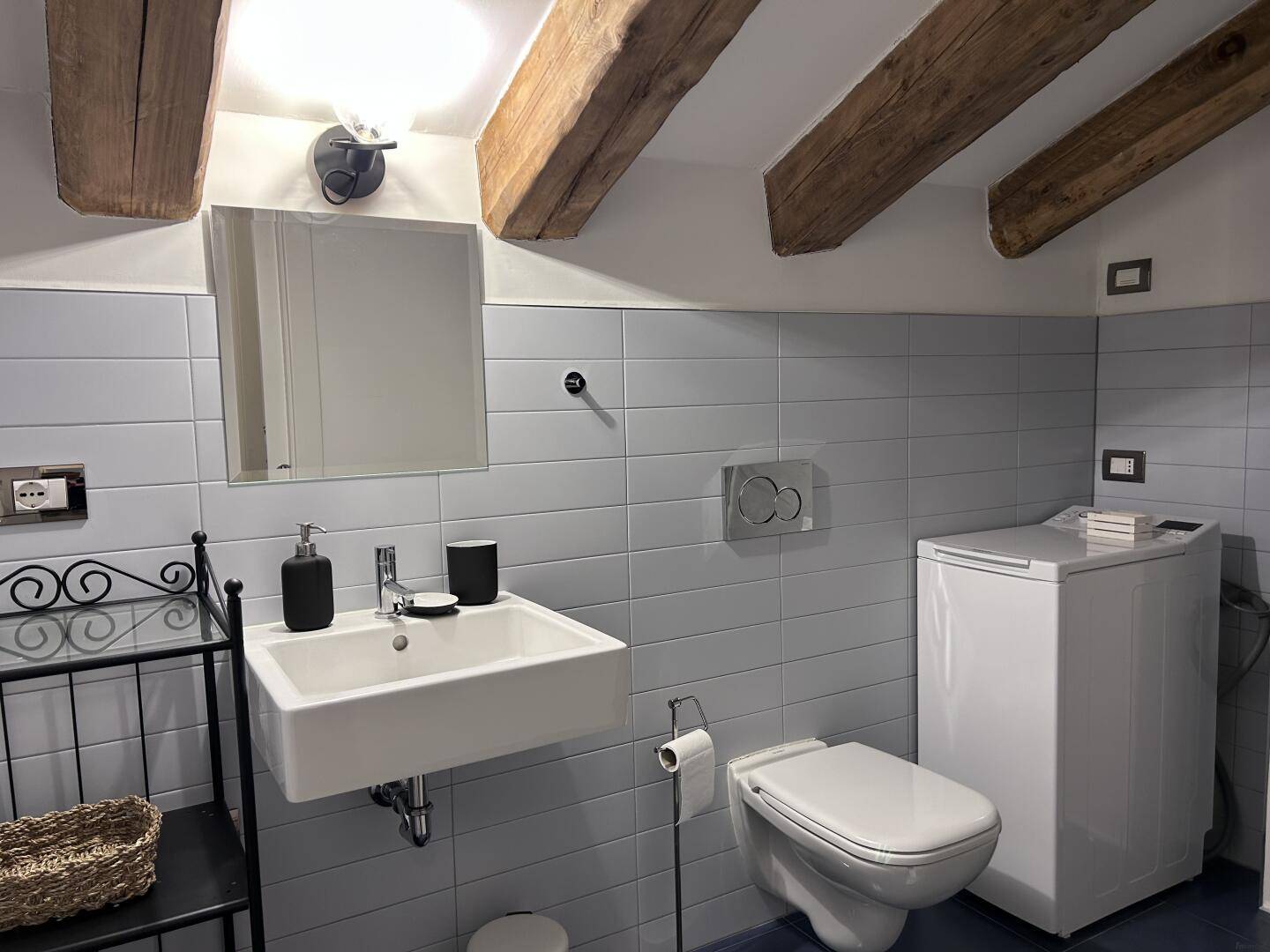 Modernes Badezimmer mit hellblauen Fliesen, Waschbecken und wandhängendem WC unter Holzbalken.