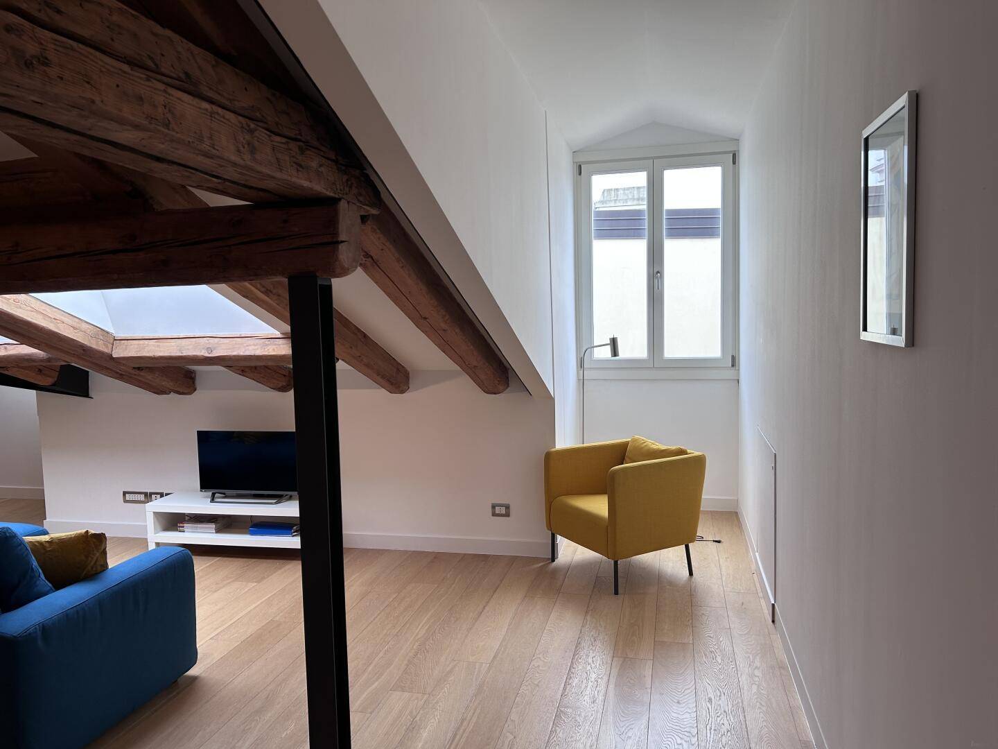 Gemütliche Sitzecke mit gelbem Sessel, Holzbalken und einem hohen Fenster für natürliches Licht.