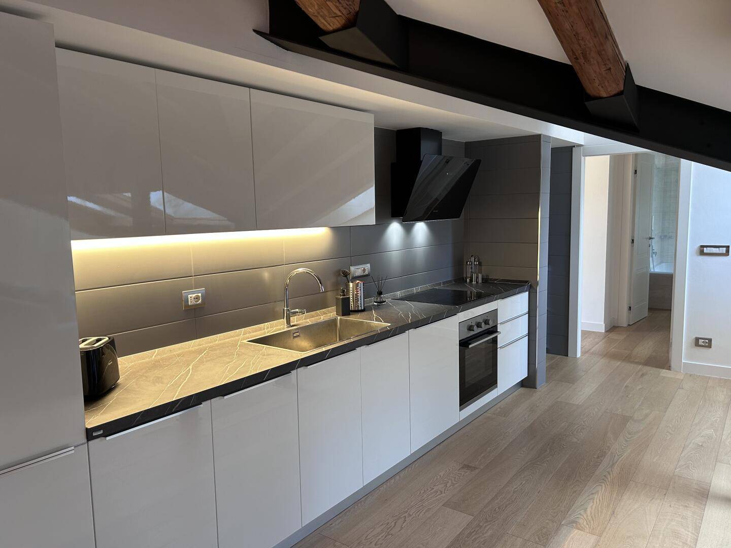 Moderne Einbauküche mit weißen Hochglanzfronten, dunkler Arbeitsplatte und integrierten Geräten.