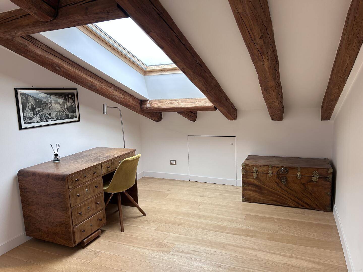 Arbeitszimmer mit Holzbalken, Parkettboden, antikem Schreibtisch und einem Dachfenster für Helligkeit.
