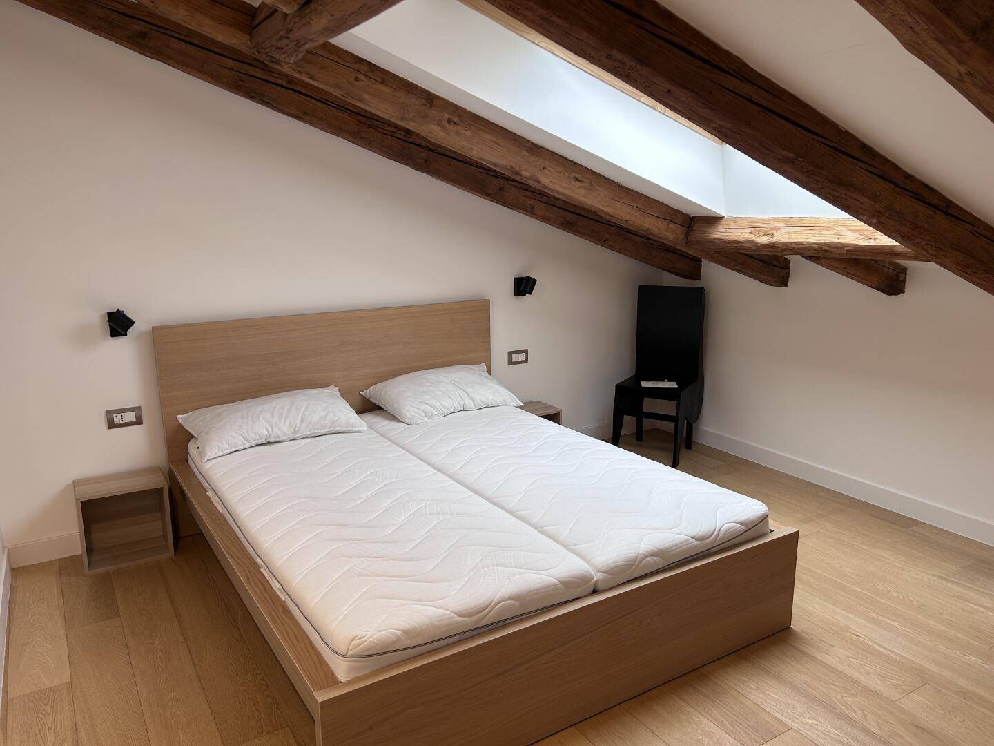 Schlafzimmer unter dem Dach mit Holzbalken, Parkettboden und einem großen Doppelbett mit Nachttischen.