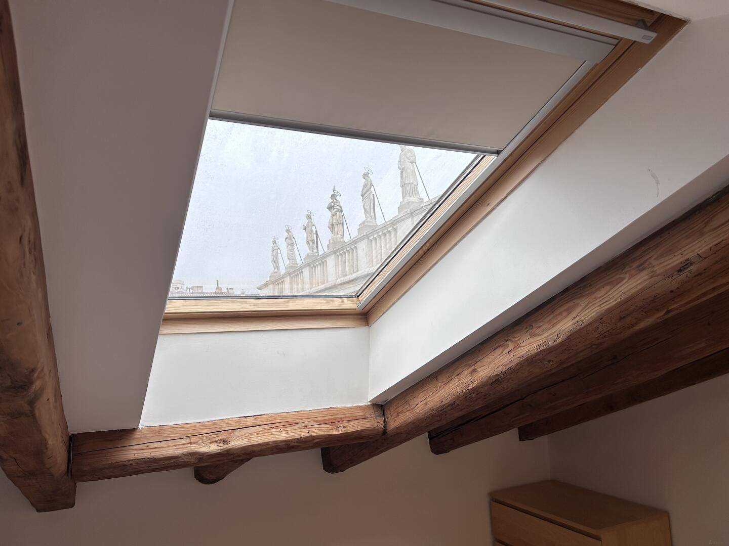 Dachfenster mit Blick auf historische Statuen und den Himmel, umgeben von rustikalen Holzbalken.