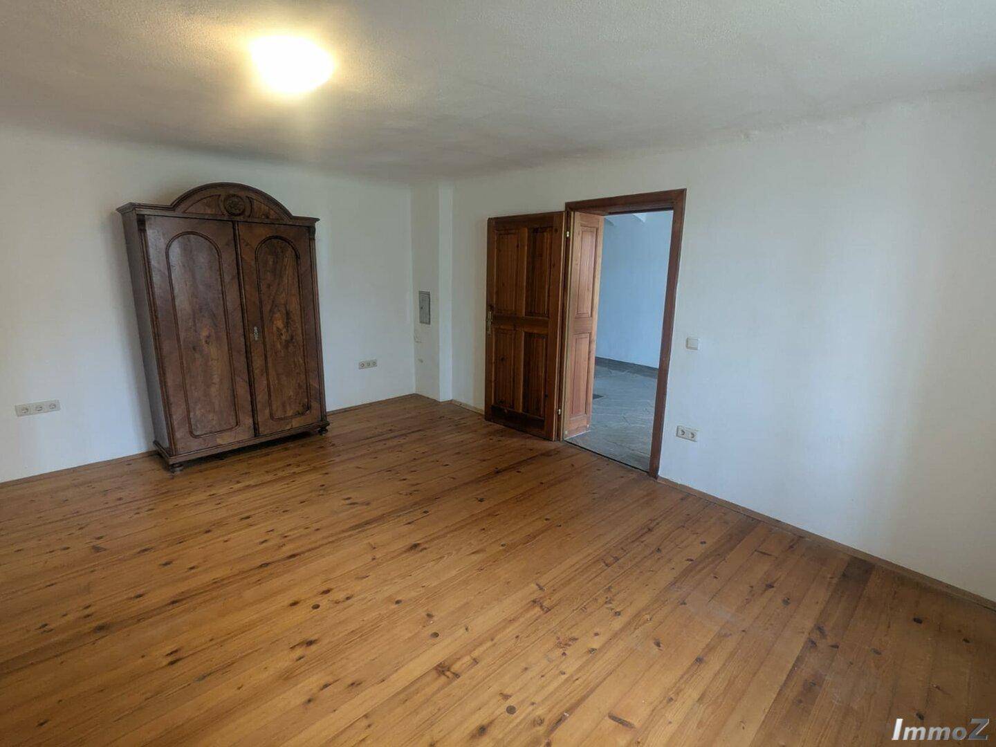 Geräumiges Zimmer mit hellem Holzfußboden und einem antiken Holzschrank.