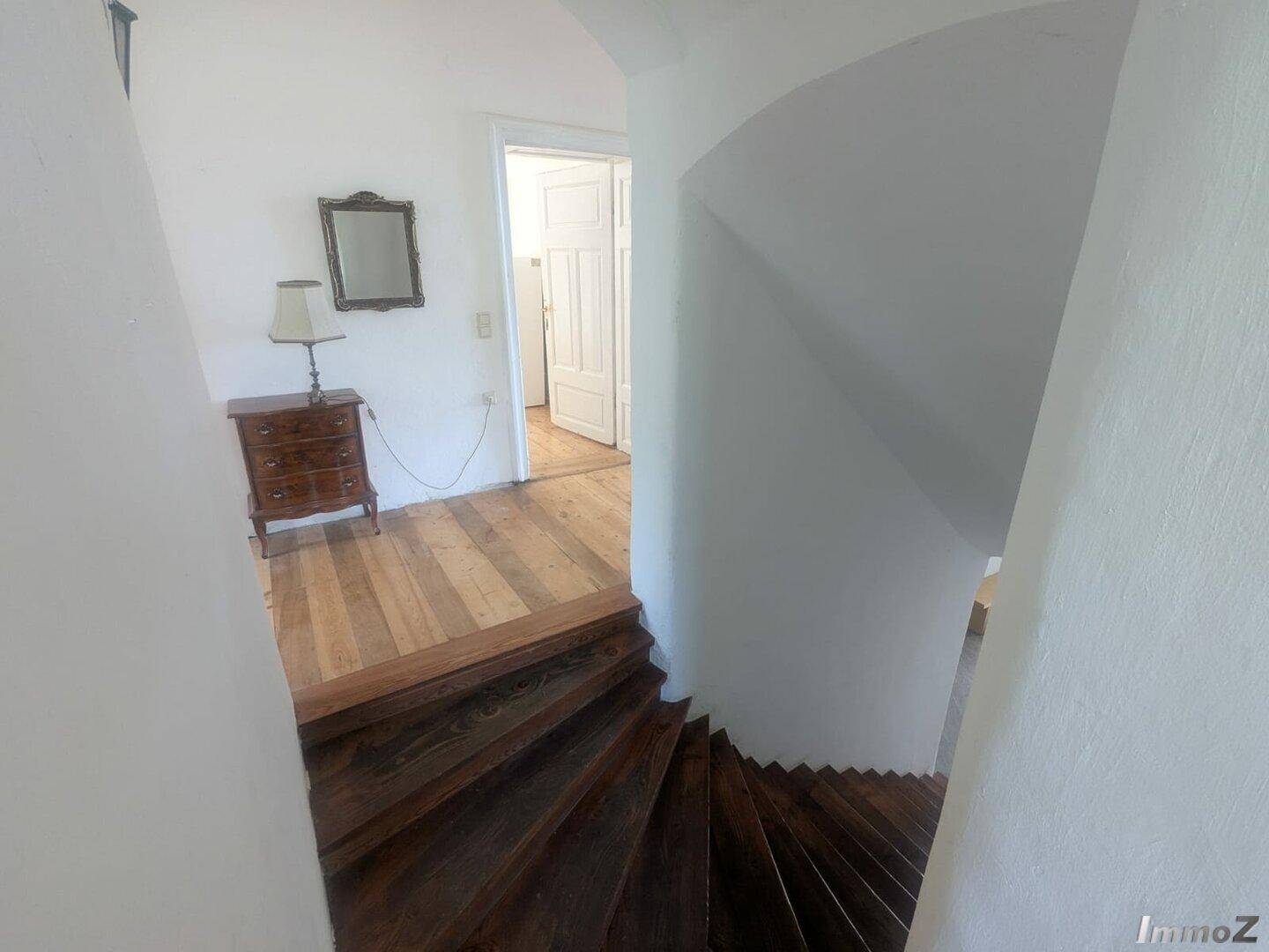 Oberer Treppenabsatz mit Holzfußboden, antiker Kommode und Blick in angrenzende Räume.
