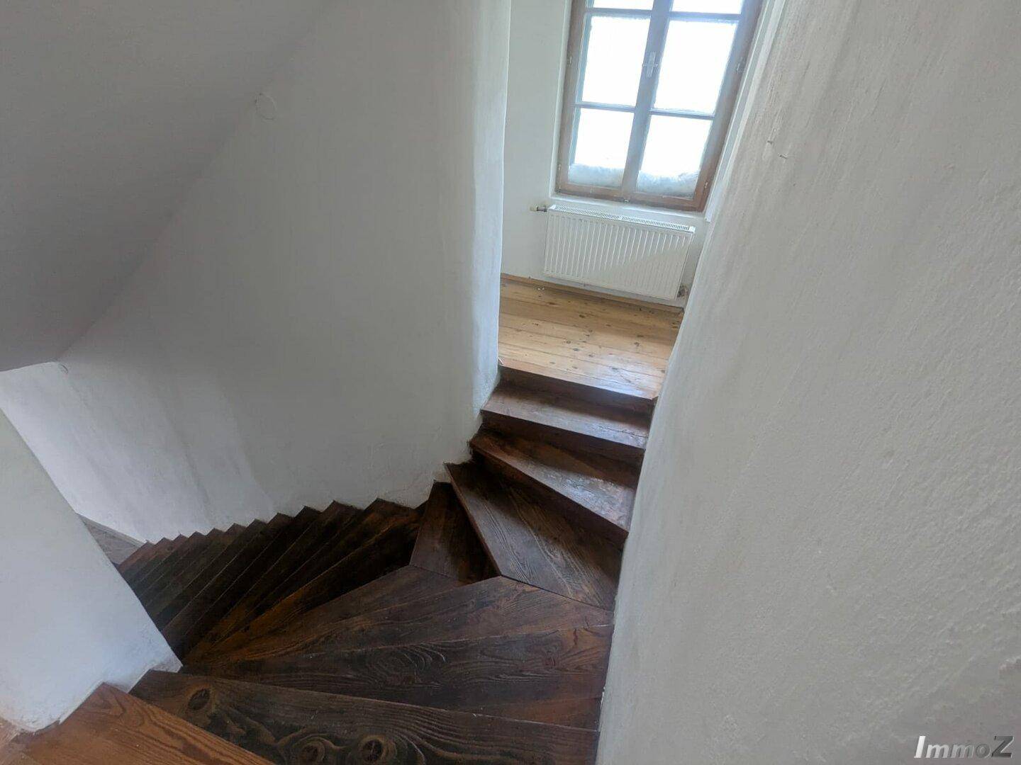 Wendeltreppe aus Holz mit weiß getünchten Wänden und einem Fenster, das Licht hereinlässt.