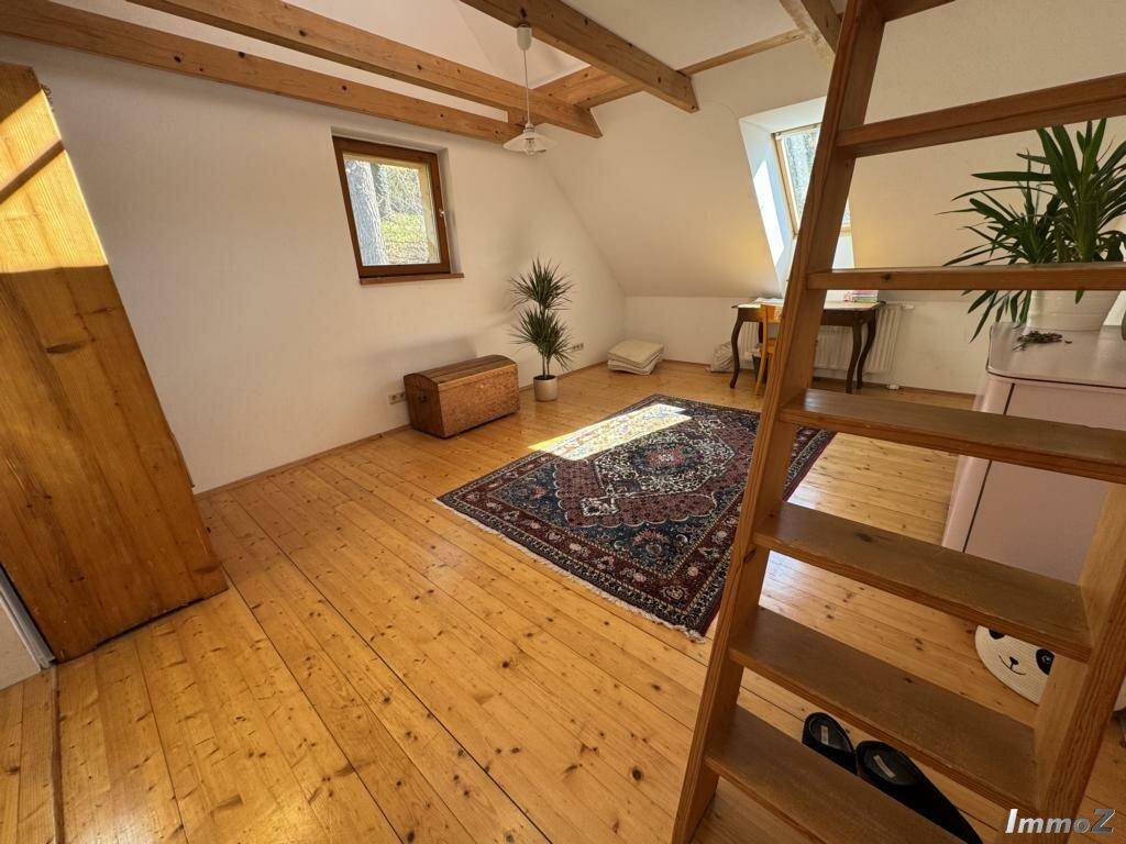 Lichtdurchflutetes Dachzimmer mit Holzdielenboden, sichtbaren Balken und einem Teppich.