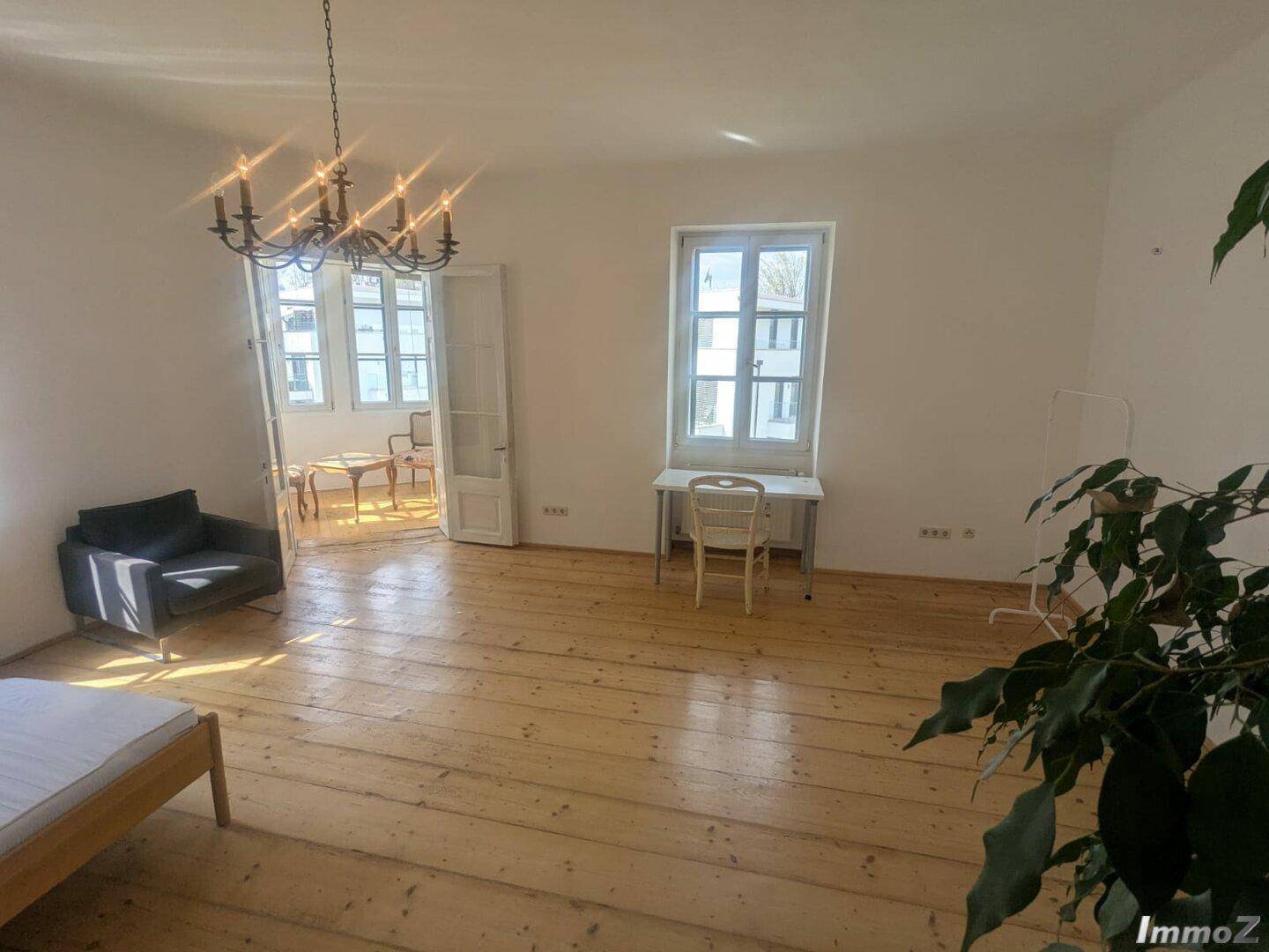 Geräumiges Wohnzimmer mit Holzdielenboden, Kronleuchter und Zugang zu einem hellen Wintergarten.