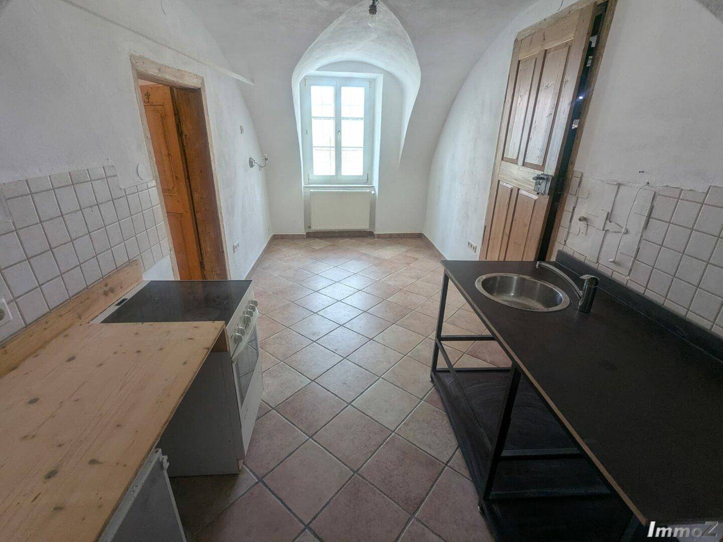 Kleine Küche mit Fliesenboden, einfacher Ausstattung und einem Fenster mit Gewölbedecke.