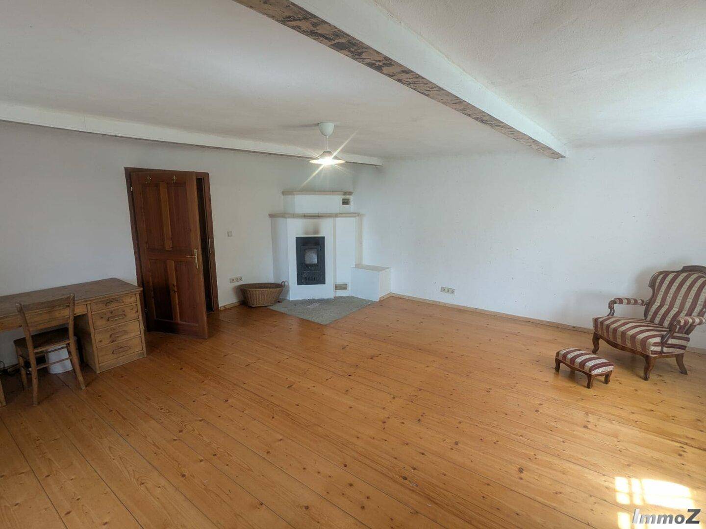 Helles Wohnzimmer mit Holzboden, Kaminofen und rustikalen Holzbalken an der Decke.