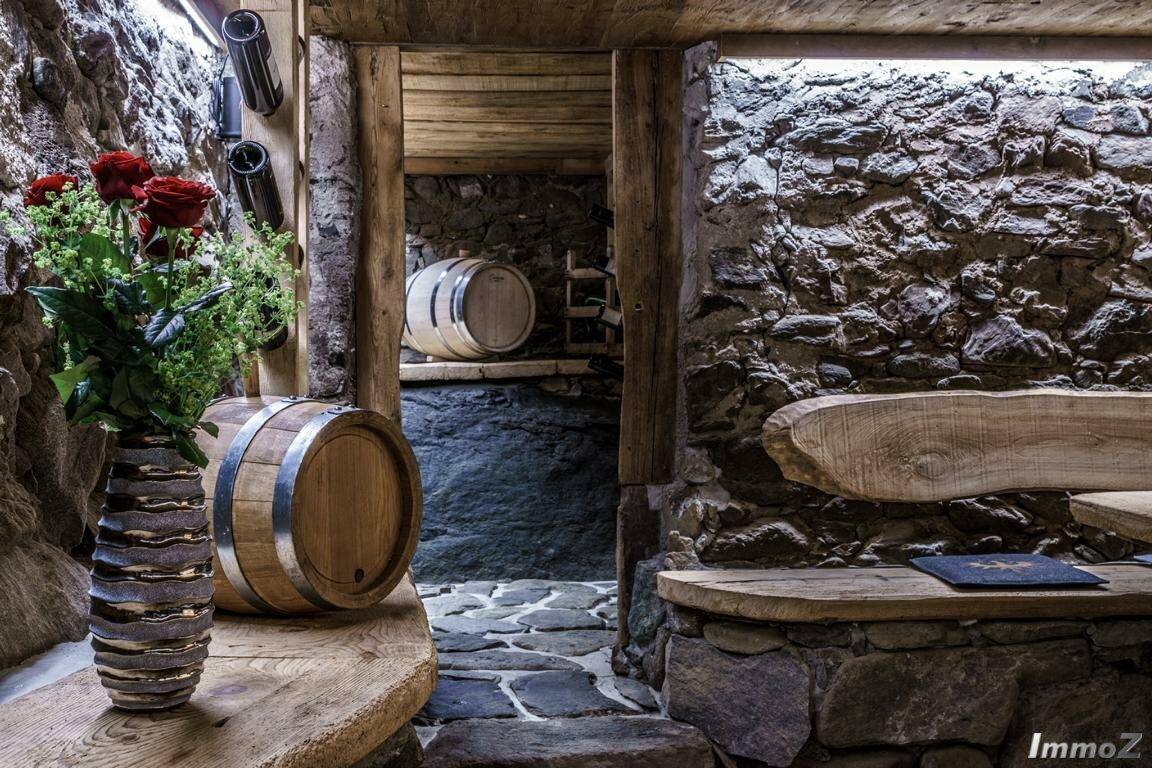 Rustikaler Weinkeller mit Steinwänden, Holzfässern und einer gemütlichen Sitzgelegenheit.