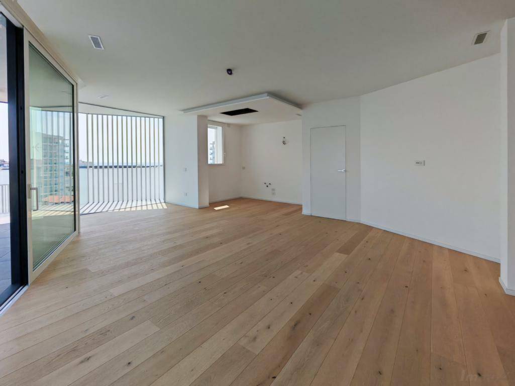 Heller, leerer Wohnraum mit Holzboden und großen Glasschiebetüren zum Außenbereich.