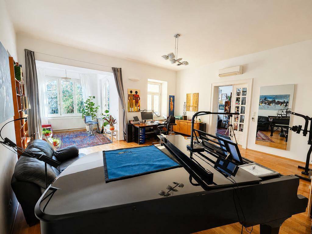 Großzügiges Wohnzimmer mit Flügel, Arbeitsbereich und Erkerfenstern für viel Licht.