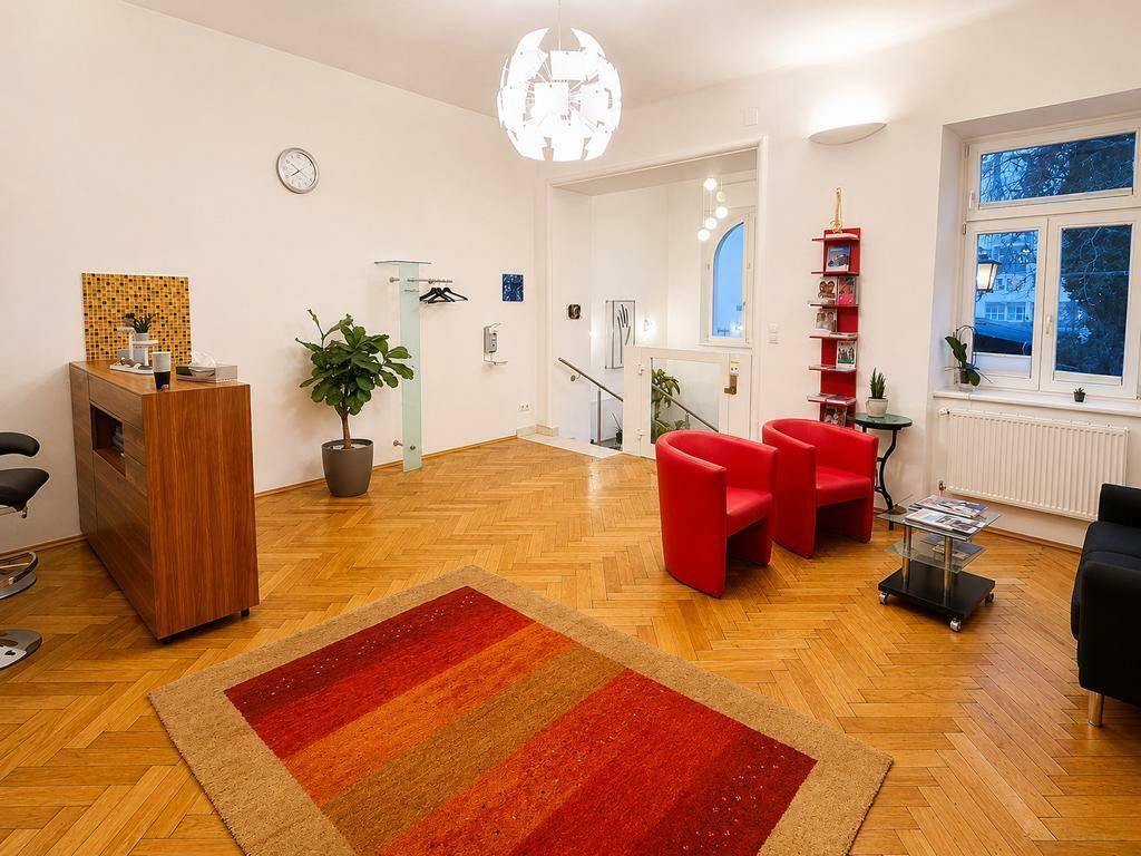 Heller Empfangsbereich mit Holzboden, roten Sesseln und Blick auf die Treppe.