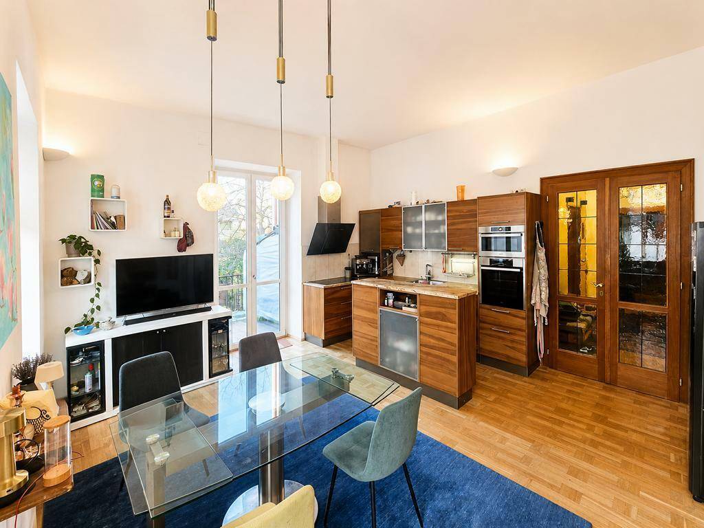 Offener Wohn-Essbereich mit moderner Holzküche, Esstisch und Zugang zum Balkon.