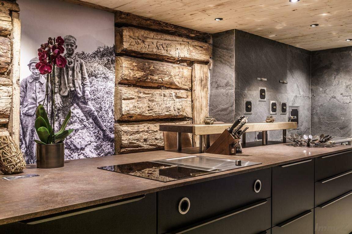 Moderne Küche im alpinen Stil mit dunklen Schränken, Holzbalken und Steinwand.