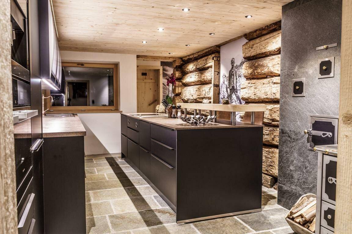 Helle Küche mit Kochinsel, Fenster und rustikalem Steinboden im alpinen Design.