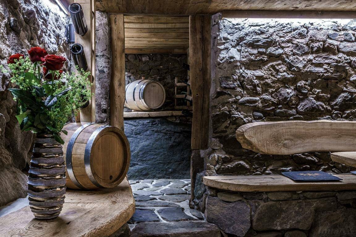 Rustikaler Weinkeller mit Steinwänden, Holzfässern und einer gemütlichen Sitzgelegenheit.
