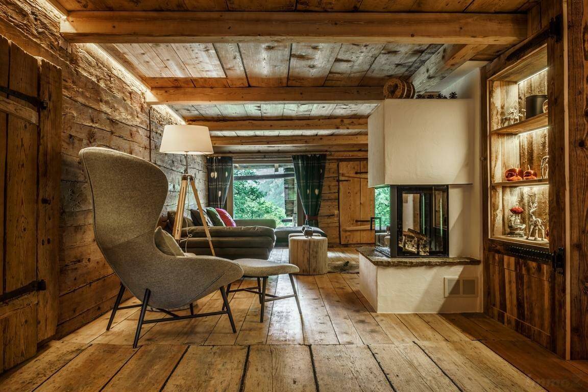Helles Wohnzimmer mit Kamin, Holzboden und großem Sessel mit Blick ins Grüne.