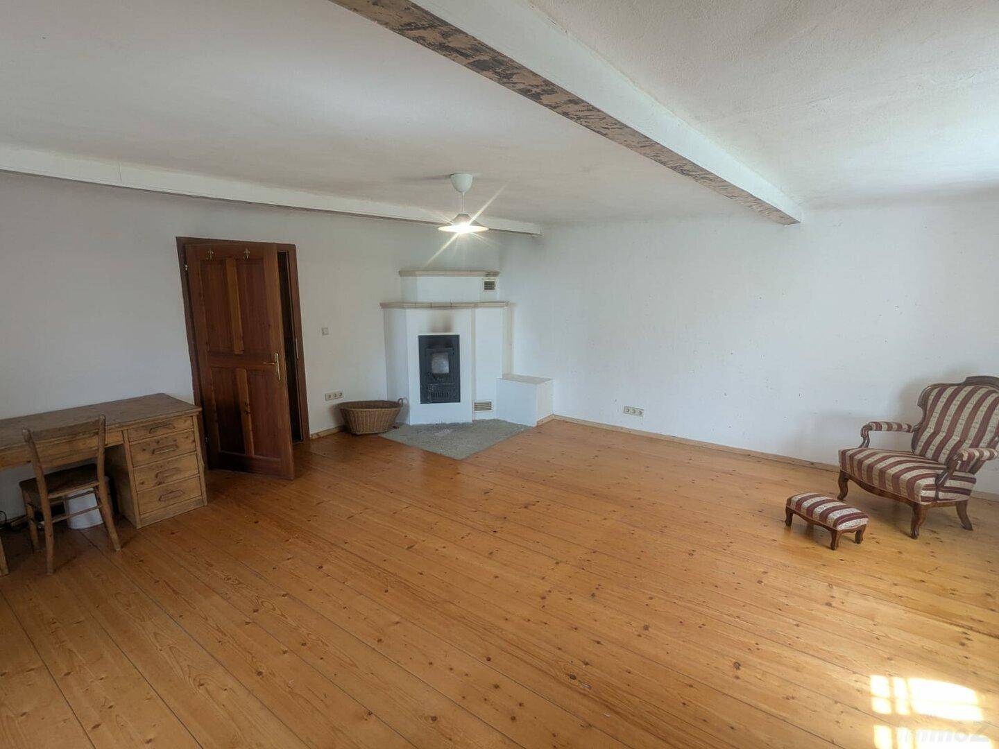 Gemütliches Wohnzimmer mit Holzdielenboden, einem Kaminofen und sichtbaren Deckenbalken.