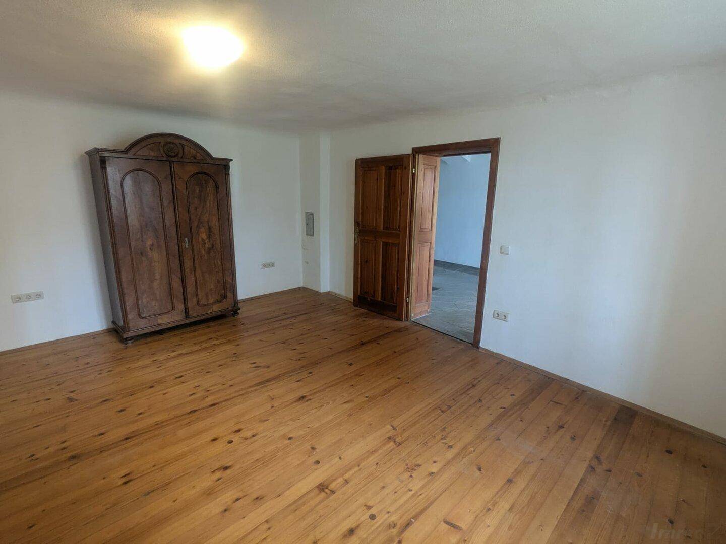 Geräumiges Schlafzimmer mit hellem Holzplankenboden und einem traditionellen Holzschrank.