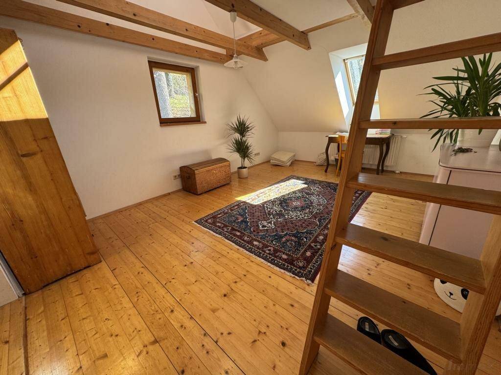 Geräumiges Dachzimmer mit Holzdielenboden, schrägen Decken und viel natürlichem Licht.