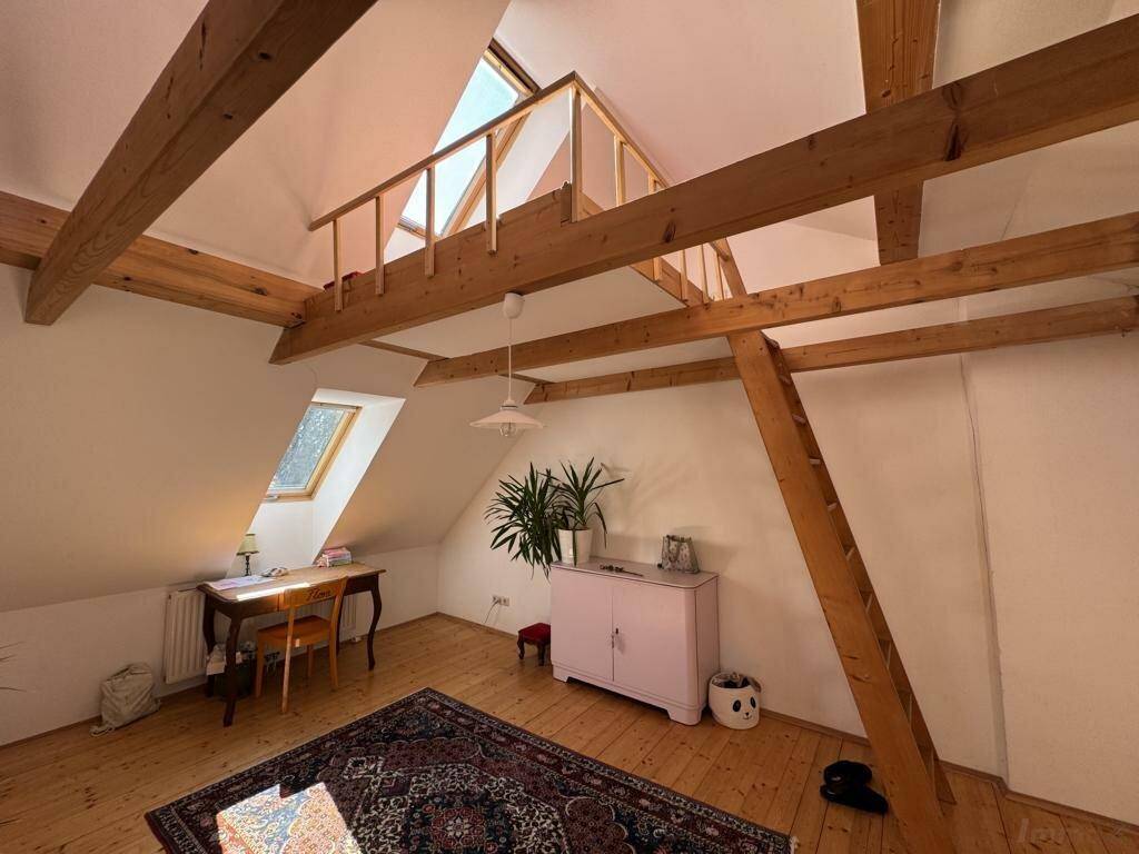Dachzimmer mit Holzdielenboden, sichtbaren Holzbalken und einer Leiter zu einer oberen Ebene.