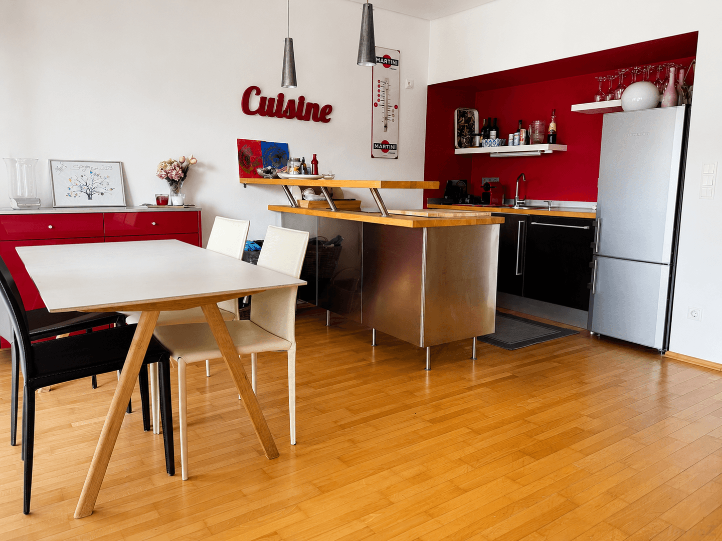 Moderne Küche mit roter Akzentwand, Edelstahl-Insel und Essbereich.